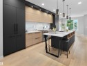 Sleek kitchen featuring light wood-finish flooring, a central island with white countertop, integrated black cabinetry, under-cabinet lighting, and subway tile backsplash - 9118 89 Street Nw, Edmonton, AB 