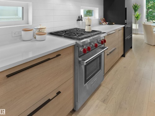 Stainless steel range with red accent knobs, white countertops, wood-finish cabinetry, and light wood-finish flooring - 9118 89 Street Nw, Edmonton, AB 