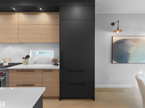 Integrated black cabinetry, light wood-finish lower and upper cabinetry, white subway tile backsplash, white countertop, and light wood-finish flooring - 9118 89 Street Nw, Edmonton, AB 