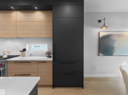 Integrated black cabinetry, light wood-finish lower and upper cabinetry, white subway tile backsplash, white countertop, and light wood-finish flooring - 