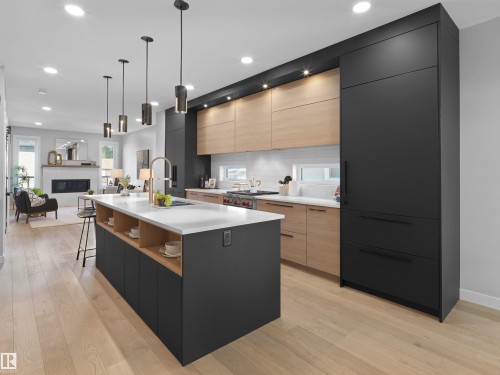 Spacious kitchen with a large central island, light wood-finish flooring, matte black and natural wood cabinetry, integrated appliances, and recessed lighting - 9118 89 Street Nw, Edmonton, AB 