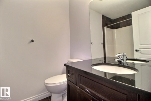 Dark wood-finish vanity with an undermount sink, dark stone-finish countertop, and polished chrome faucet - 5205 168 Avenue Nw, Edmonton, AB 