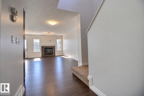 Spacious room with wood-finish flooring, a contemporary fireplace with a tile surround, and multiple windows - 5205 168 Avenue Nw, Edmonton, AB 