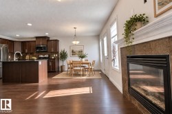 Open-concept living space with wood-finish flooring, a kitchen island, dark wood cabinetry, a built-in fireplace with tile surround, and multiple windows - 