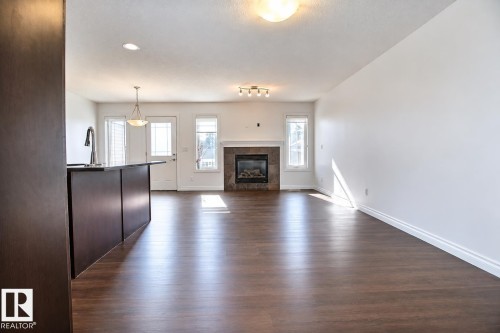 Wood-finish flooring, built-in fireplace with stone surround, white walls, recessed lighting, and a breakfast bar with dark cabinetry - 5205 168 Avenue Nw, Edmonton, AB 