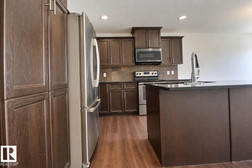 Kitchen featuring dark wood-finish cabinetry, stainless steel appliances, dark countertops, and wood-finish flooring - 5205 168 Avenue Nw, Edmonton, AB 