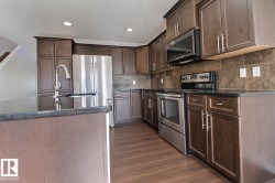Kitchen featuring dark wood-finish cabinetry, stainless steel appliances, dark countertops, a large kitchen island with an integrated sink, and wood-finish flooring - 