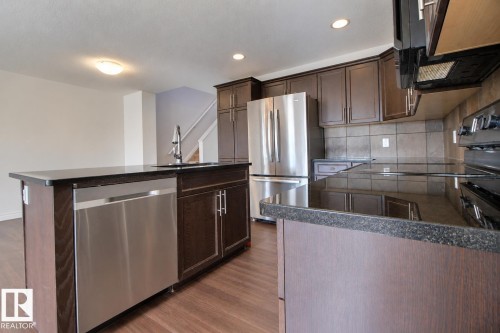 Kitchen featuring dark wood-finish cabinetry, stainless steel appliances, dark stone countertops, and a tile backsplash - 5205 168 Avenue Nw, Edmonton, AB 
