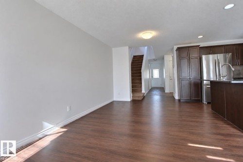 Wood-finish flooring, staircase with carpeted treads, built-in kitchen cabinetry, stainless steel refrigerator, and a kitchen island with an integrated sink - 5205 168 Avenue Nw, Edmonton, AB 