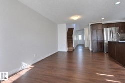 Wood-finish flooring, staircase with carpeted treads, built-in kitchen cabinetry, stainless steel refrigerator, and a kitchen island with an integrated sink - 