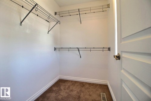 Walk-in closet with carpet flooring, wire shelving, and a white paneled door with a brass-finish knob - 5205 168 Avenue Nw, Edmonton, AB 