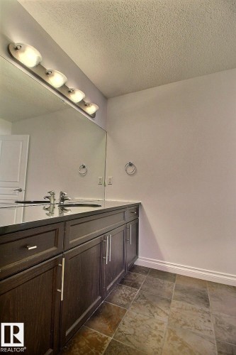 Dark wood finish vanity with integrated sink, dark countertop, full wall-mounted mirror, and multi-bulb vanity lighting - 5205 168 Avenue Nw, Edmonton, AB 