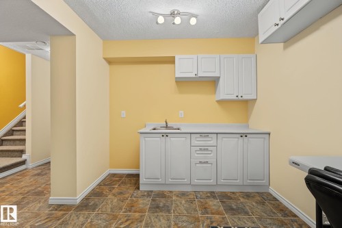 Built-in kitchenette with white cabinetry, light-toned countertop, and stainless steel sink - 5205 168 Avenue Nw, Edmonton, AB 
