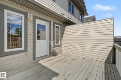 Exterior deck with wood planks, featuring a privacy wall, a white exterior door with glass inserts, and two large windows with white frames - 