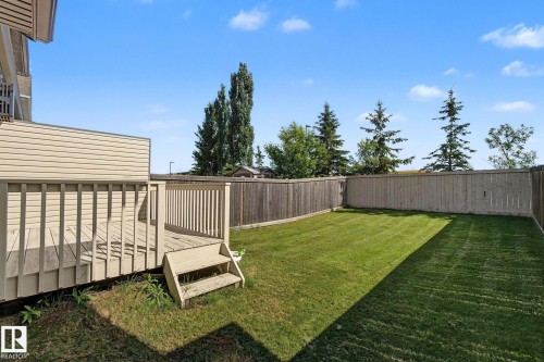 Expansive fenced yard featuring a spacious wood deck with stairs, a large grassy area, and mature perimeter trees - 5205 168 Avenue Nw, Edmonton, AB 