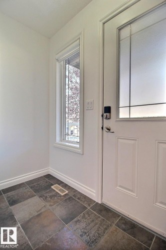 Entryway with multi-toned tile flooring, a white paneled door with decorative frosted glass, and a side window with gridded panes - 5205 168 Avenue Nw, Edmonton, AB 