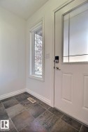 Entryway with multi-toned tile flooring, a white paneled door with decorative frosted glass, and a side window with gridded panes - 