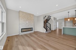 Spacious room featuring wood-finish flooring, a stone-clad fireplace with a linear insert, recessed lighting, a staircase with black metal balusters, and a kitchen island with a light-colored countertop - 