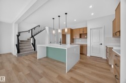 White waterfall-edge kitchen island, wood-finish flooring, recessed lighting, wood cabinetry, and a carpeted staircase with dark railings - 
