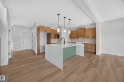 Open-concept kitchen with wood-finish flooring, light wood cabinetry, quartz waterfall island, and recessed lighting - 