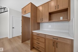 Wood-finish cabinetry with black hardware, white countertops, and a white mosaic tile backsplash - 