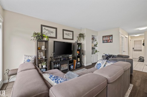 Wood-finish flooring throughout, with neutral wall tones, built-in shelving, and a double French door entry - #63 501 Youville Dr E Nw, Edmonton, AB 