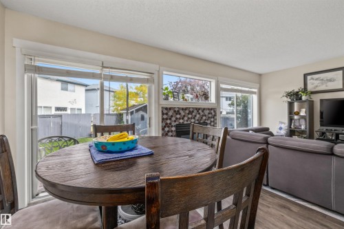 Sliding glass door to the backyard, multiple windows, fireplace with decorative tile surround, and wood-finish flooring - #63 501 Youville Dr E Nw, Edmonton, AB 