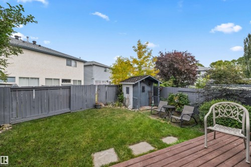Expansive backyard featuring a wood-finish deck, a detached storage shed, privacy fencing, and a manicured lawn with stepping stones - #63 501 Youville Dr E Nw, Edmonton, AB 