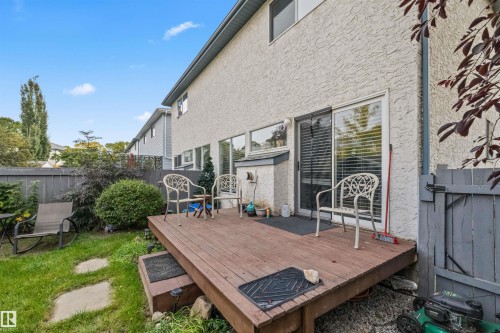 Exterior stucco siding featuring a wood deck with steps, a sliding glass door, and a privacy fence - #63 501 Youville Dr E Nw, Edmonton, AB 