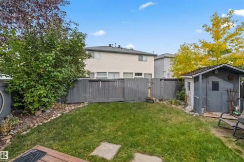 Expansive fenced backyard featuring a manicured lawn, established shrubbery, and a storage shed - #63 501 Youville Dr E Nw, Edmonton, AB 