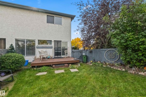 Private backyard with a raised wood deck, mature landscaping, and a privacy fence - #63 501 Youville Dr E Nw, Edmonton, AB 