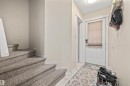 Carpeted staircase with white trim, leading to a hallway with tiled flooring and a white entry door - #63 501 Youville Dr E Nw, Edmonton, AB 