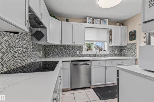 White cabinetry, herringbone tile backsplash, integrated cooktop, stainless steel dishwasher, and a single basin sink with a gooseneck faucet - #63 501 Youville Dr E Nw, Edmonton, AB 
