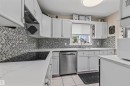 White cabinetry, herringbone tile backsplash, integrated cooktop, stainless steel dishwasher, and a single basin sink with a gooseneck faucet - #63 501 Youville Dr E Nw, Edmonton, AB 