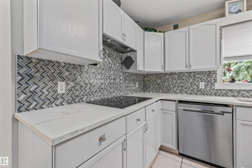 White cabinetry, herringbone tile backsplash, white countertops, built-in cooktop, and stainless steel dishwasher - #63 501 Youville Dr E Nw, Edmonton, AB 