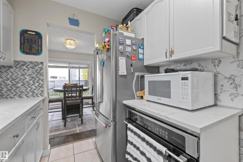 Galley kitchen featuring white cabinetry, light-toned countertops, and a chevron pattern tile backsplash - #63 501 Youville Dr E Nw, Edmonton, AB 