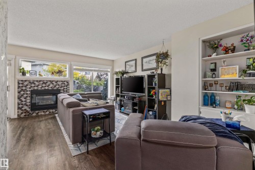 Wood-finish flooring, built-in shelving, fireplace with hexagon tile surround, and multiple windows - #63 501 Youville Dr E Nw, Edmonton, AB 