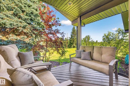 Covered outdoor patio featuring a slatted wood-finish deck, overhead recessed lighting, and a verdant backdrop of mature trees and landscaping - 22245 Twp Road 512, Rural Strathcona County, AB 