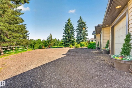 Spacious gravel driveway with a wood fence bordering a treed area - 22245 Twp Road 512, Rural Strathcona County, AB 