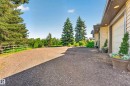 Spacious gravel driveway with a wood fence bordering a treed area - 22245 Twp Road 512, Rural Strathcona County, AB 