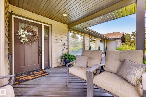 Covered front porch featuring a paneled entry door with sidelight, horizontal siding, recessed lighting, and a composite deck - 22245 Twp Road 512, Rural Strathcona County, AB 