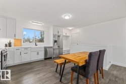 Kitchen featuring white shaker-style cabinetry, wood-finish flooring, stainless steel appliances, a farmhouse-style apron sink, and built-in storage - 
