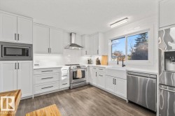 Kitchen featuring white shaker-style cabinetry, stainless steel appliances, a white farmhouse sink with a black faucet, white subway tile backsplash, and wood-finish flooring - 