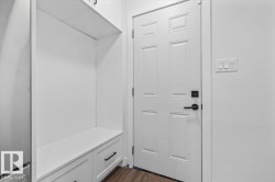 Built-in white storage cabinetry with drawers, six-panel door with matte black hardware, and wood-finish flooring - 