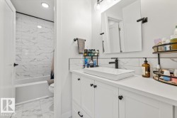 White vanity cabinet featuring a rectangular vessel sink and matte black faucet, accompanied by a tub shower with white tile surround and natural stone-patterned floor tile - 