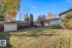 Expansive backyard featuring a sprawling lawn, mature trees, perimeter wood fencing, and a detached storage structure with siding - 