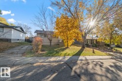 Single-story exterior featuring light-colored horizontal siding, a concrete driveway, and mature trees on a level lot - 