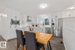 Kitchen featuring white shaker cabinetry, stainless steel appliances, apron-front sink, chimney-style range hood, and wood-finish flooring - 