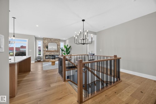 Hardwood flooring, wrought iron railing, stone fireplace, recessed lighting, and a modern chandelier - 209 Hampshire, Sherwood Park, AB 