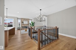 Hardwood flooring, wrought iron railing, stone fireplace, recessed lighting, and a modern chandelier - 